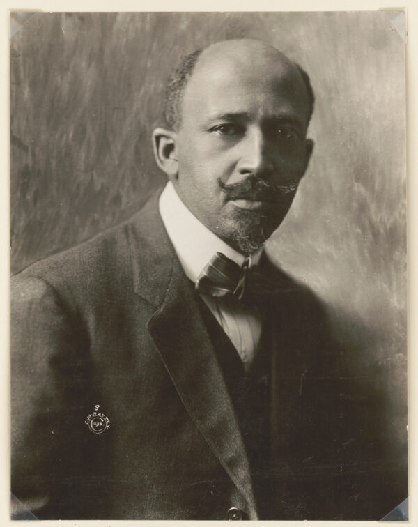 A photo of a middle-aged Black man with a receding hairline and a well-groomed moustache wearing a suit jacket, sweater vest, and bow tie.