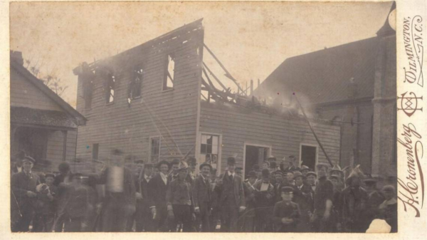 Crowd of people stand in front of a building that seems to be about half burned down.