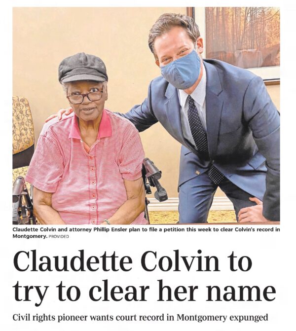 A newspaper clipping showing an older Black woman seated in a wheelchair with a younger white man wearing a suit and a face mask standing beside her.