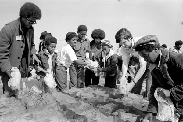 A group of volunteers, mostly young and Black, fill grocery bags with whole chickens.