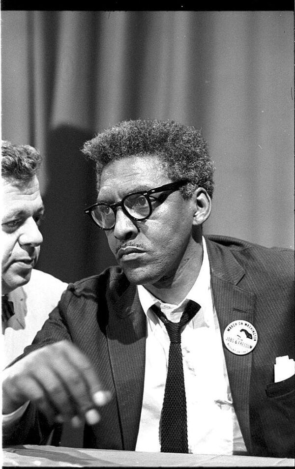 A half-length portrait of a Black man with medium length salt and pepper hair wearing a suit and tie with a 