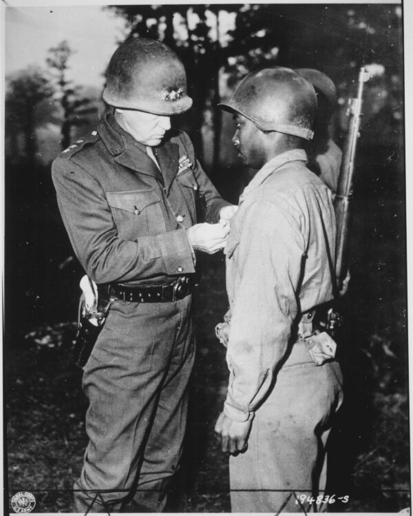 A uniformed white officer pins a medal on the uniform of a young Black soldier.