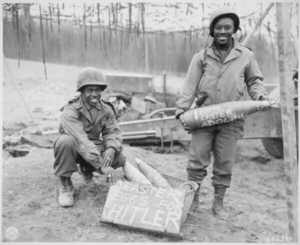 Two uniformed Black soldiers smile as one holds up a sign that reads 