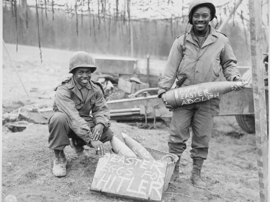Two uniformed Black soldiers smile as one holds up a sign that reads 