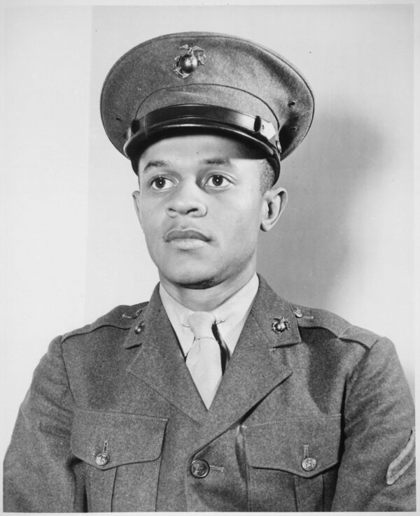 Photograph of a young Black man wearing a military uniform that includes a jacket and cap, both with pins that feature a globe with an eagle on top.