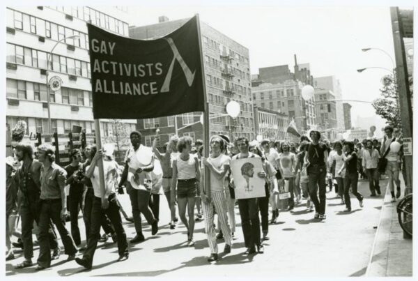 A group of people are marching in a parade while holding a large sign that reads 