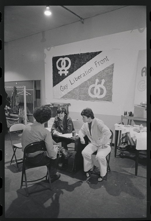 Three people sitting at a table in front of a large banner hung on the wall that reads 
