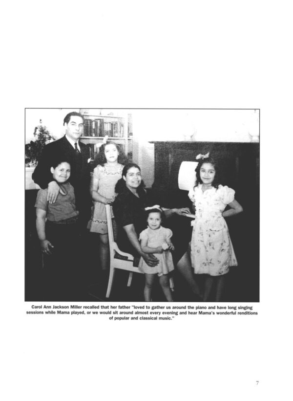 A mother, father, and four children sit and stand together in front of a piano and a bookcase wearing their Sunday best.