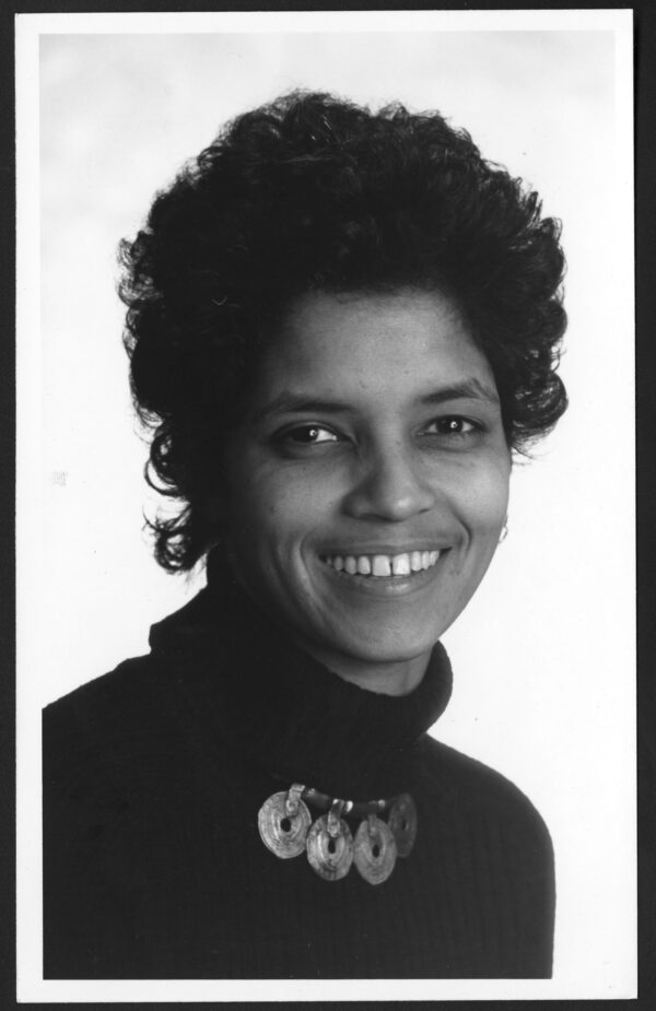 A Black woman with short dark hair wearing a dark turtleneck looks into the camera and smiles in a posed portrait.