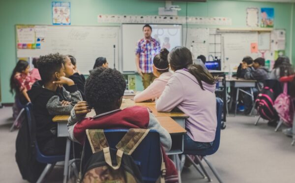 A teacher instructing a diverse group of students in a classroom.