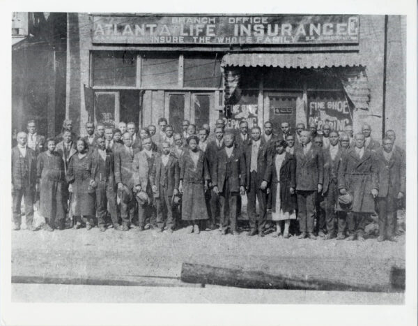 Historical black and white photograph of a large group of African American men and women standing in front of the Atlanta Life Insurance Company branch office. The building has visible signage reading 