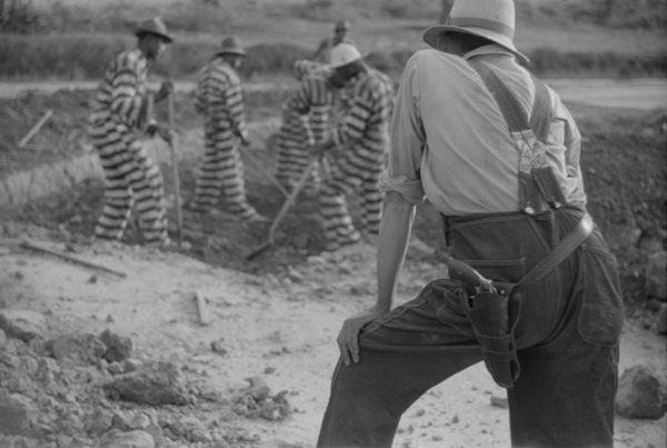 Group of incarcerated Black men in striped uniforms digging with tools under the watch of an armed guard in Oglethorpe County, Georgia