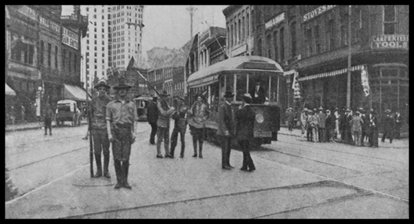 State militia and armed men standing in the street near a streetcar at the intersection of Walton and Peachtree Streets in Atlanta during the 1906 race massacre, with onlookers gathered along the sidewalks
