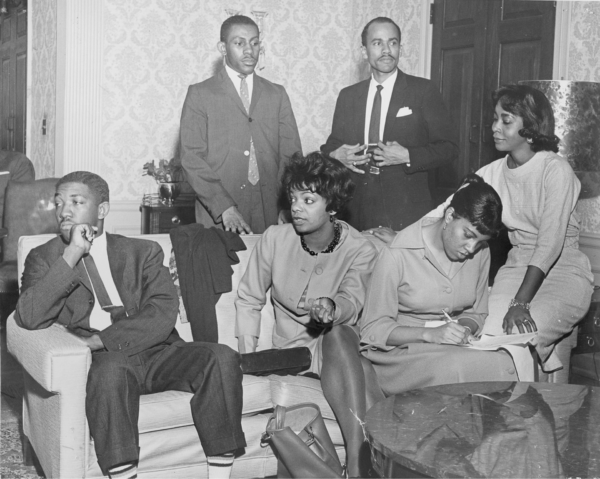 Members of the Committee on the Appeal for Human Rights meeting in Atlanta, 1961, seated and standing in a living room, with one woman writing notes while others listen and speak